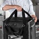 A chef holding a black Vollrath 3-Series insulated tower bag.