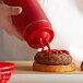 A person using a Vollrath Twin Tip Squeeze Bottle to pour ketchup onto a hamburger.