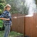 A woman using a Simpson Megashot pressure washer to spray a wooden fence.
