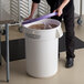 A person using a purple lid to cover a white Baker's Mark ingredient storage bin full of brown grains.