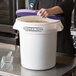 A woman holding a white Baker's Mark ingredient storage bin with a purple lid.