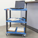 A blue Luxor utility cart with a laptop on a shelf.