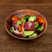An Elite Global Solutions round bamboo and melamine bowl filled with salad on a wood table.