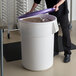 A person putting a purple lid on a white ingredient storage bin full of grains.