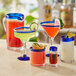 A table with Acopa Tropic cooler glasses with blue rims filled with different colored drinks.