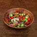 An Elite Global Solutions round bamboo and melamine bowl filled with a salad of cucumbers, tomatoes, onions, and other vegetables.