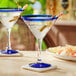 Two Acopa martini glasses with blue rims filled with blue liquid on a white table.