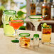 A variety of Acopa Tropic martini glasses with green rims and bases filled with different colored drinks on a table.