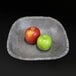 A rectangular coal colored stone bowl filled with a red and green apple.
