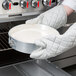 A person using white gloves to remove a Chicago Metallic springform cake pan from the oven.