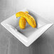 A white square melamine serving bowl filled with yellow squash.