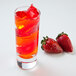 A Libbey cordial glass filled with orange liquid next to strawberries.