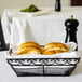 A Tablecraft black metal rectangular basket with rolls on a table.