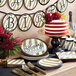 A stack of black and gold "Happy Birthday" paper plates on a table with a birthday cake.