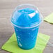 A clear plastic squat dome lid with a blue straw in a plastic cup with a blue slushy.