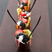 A row of WNA Comet black plastic tasting spoons in chocolate cups filled with fruit.