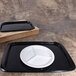 A black rectangular bamboo tray with a white plate on it.