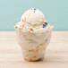 A clear Fabri-Kal sundae cup with a scoop of ice cream and sprinkles.