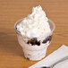 A clear PET Fabri-Kal sundae cup filled with ice cream, whipped cream, and chocolate syrup with a spoon in it.