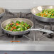 A Vollrath Wear-Ever aluminum non-stick fry pan with a bowl of vegetables on a stove.
