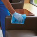 A person in blue gloves using a Rubbermaid blue microfiber cloth to clean a chair.