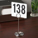 An American Metalcraft chrome swirl base table card holder with a white sign and black numbers sitting on a table.