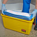A man in blue gloves using a yellow Rubbermaid container to charge a cleaning cloth.