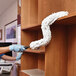 A person cleaning a shelf with a Rubbermaid White Microfiber Dusting Sleeve.
