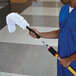 A man in blue scrubs using a white Rubbermaid dusting sleeve on a mop.