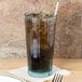 A Cambro Azure Blue polycarbonate tumbler filled with ice and cola with a straw on a napkin.