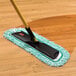 A Rubbermaid green microfiber fringed dust mop pad on a wood floor.