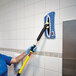 A woman in blue gloves using a Rubbermaid blue microfiber Wet Mop Pad to clean a tile wall.