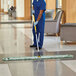 A man in a blue uniform using a Rubbermaid green microfiber fringed dust mop to clean the floor in a hospital cafeteria.