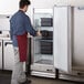 A man in an apron opening a white Avantco reach-in freezer.