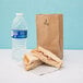 A sandwich and a Duro brown paper bag with a bottle of water inside.