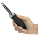 A hand holding a black and silver OXO Good Grips vegetable peeler with a straight stainless steel blade.