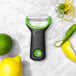 An OXO Good Grips citrus peeler with a green and yellow handle next to lemons and limes.