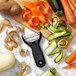 A black OXO Good Grips "Y" vegetable peeler peeling a carrot on a cutting board.