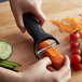 A hand uses a black OXO "Y" vegetable peeler to peel a carrot on a kitchen counter.