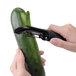 A hand holding an OXO Good Grips straight vegetable peeler and peeling a cucumber.