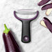 An OXO stainless steel "Y" vegetable peeler next to a purple eggplant.