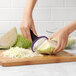A hand holding an OXO "Y" vegetable peeler peeling a piece of cabbage.