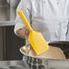 A person in a white coat mixing dough in a bowl with a Carlisle yellow paddle.