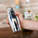 A hand holding a Vollrath stainless steel cocktail shaker.