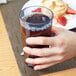 A hand holding a Cambro Newport slate blue plastic tumbler filled with brown liquid.