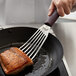 A person using a Mercer Hell's Handle Left-Handed Fish Turner to cook a piece of salmon.