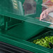 A hand using a green Cambro Versa Well Cover to put food in a container on a salad bar counter.