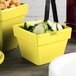 A yellow Tablecraft square container with cucumbers and crackers on a counter.