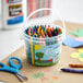 A white bucket filled with Choice school crayons on a table.