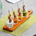 An Acopa wood flight paddle holding six small glass carafes filled with different sauces on a table.